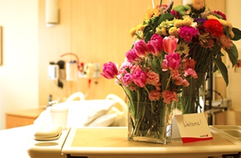 Flowers in a vase next to a hospital bed.
